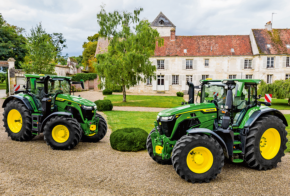 Zwei 6R John Deere Traktoren vor einem hübschen alten Gutshofsgebäude